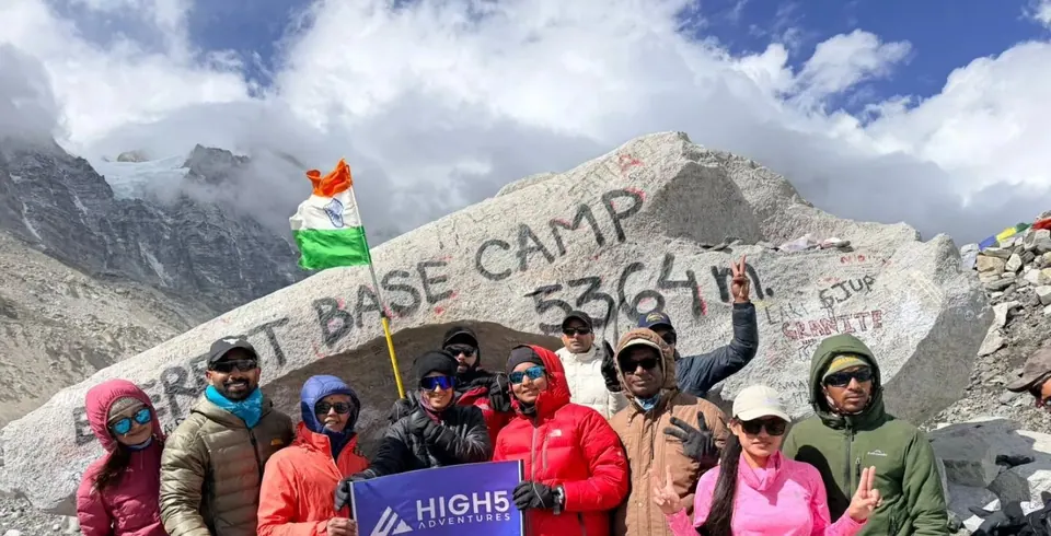 Trekkers holding a High 5 Adventures banner, with an Indian flag, in front of the painted 5,364 m boulder at Everest Base Camp, May 2026