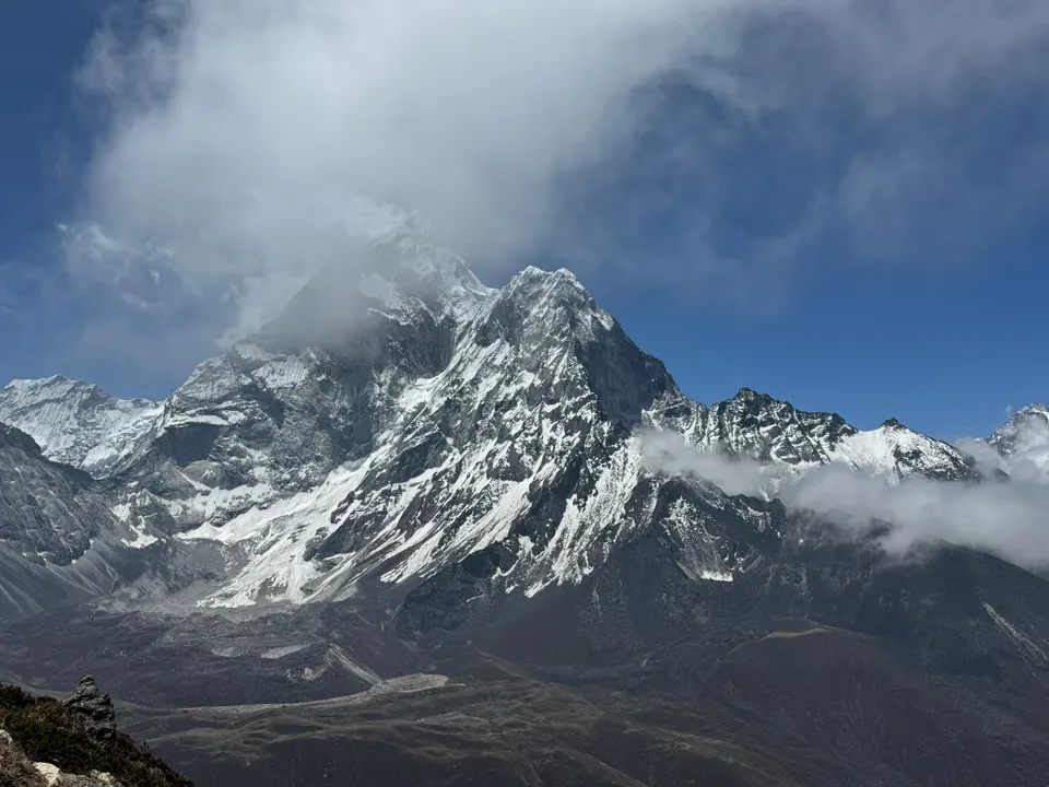 A jagged snow and rock peak with cloud streaming from its summit, above a dark valley, seen from Kala Patthar, May 2026