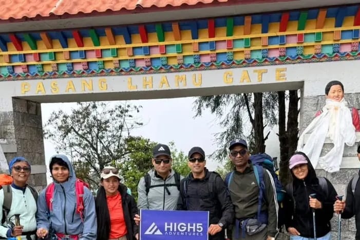 Trekkers holding a High 5 Adventures banner under the Pasang Lhamu Gate in Lukla, May 2026