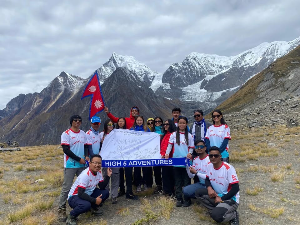 Trekkers in team T-shirts with a Nepal flag, a High 5 Adventures scarf and a signed banner, Annapurna North Base Camp, October 2025